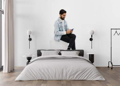 Young man sitting on chair while looking at phone celebrating on white background Wall mural